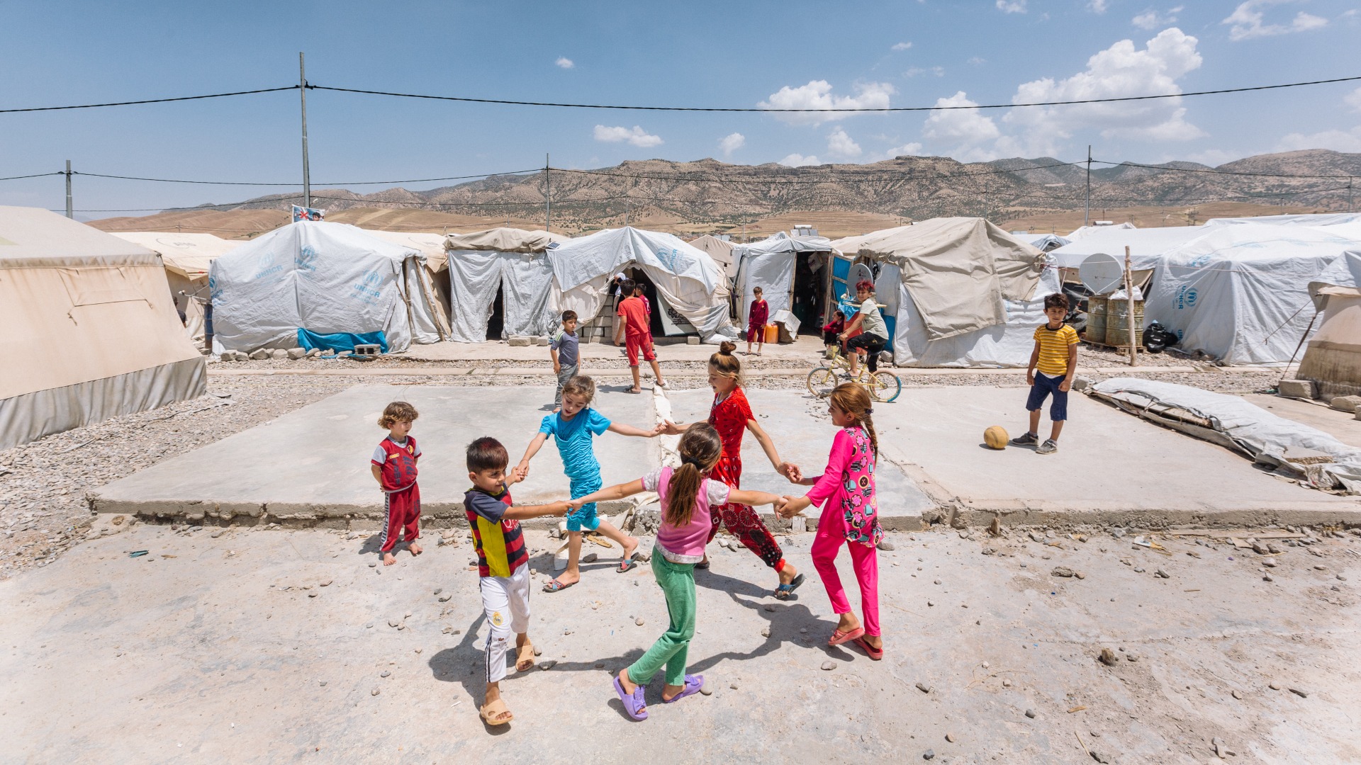 In a displacement camp in Iraq, children hold hands in a circle and play together.