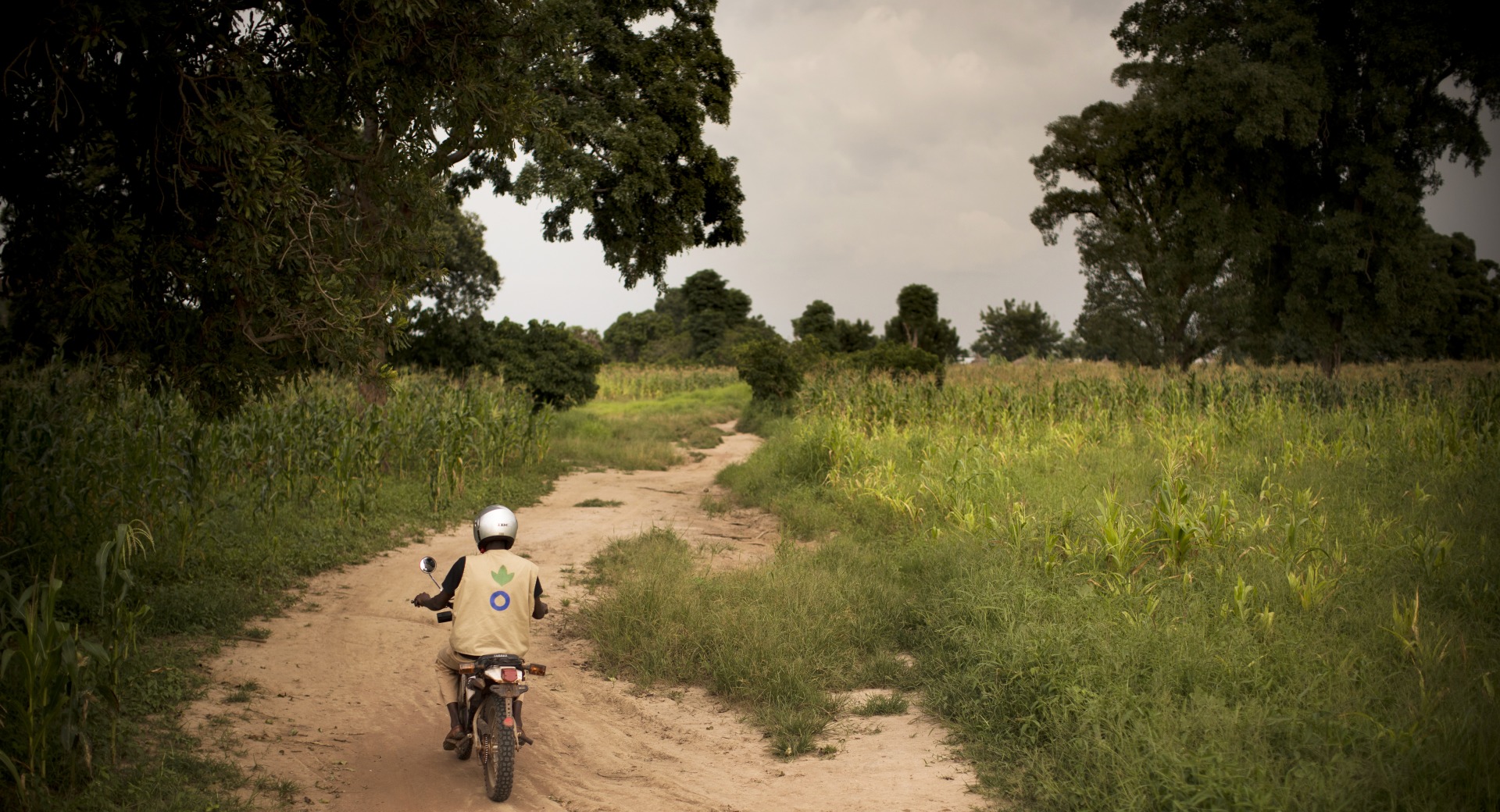 An Action Against Hunger aid worker drives a motorbike down a dirt road in Mali